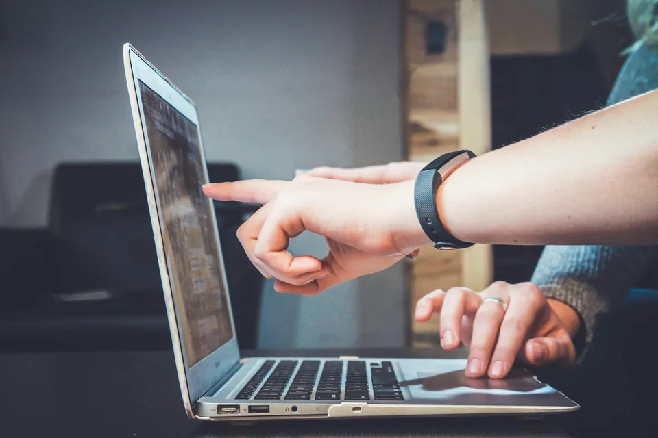 Duas pessoas observam o ecrã de um computador portátil.